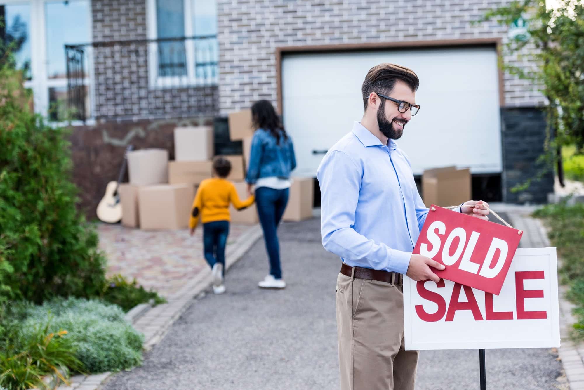 realtor hanging sold sign in front of people moving into new house
